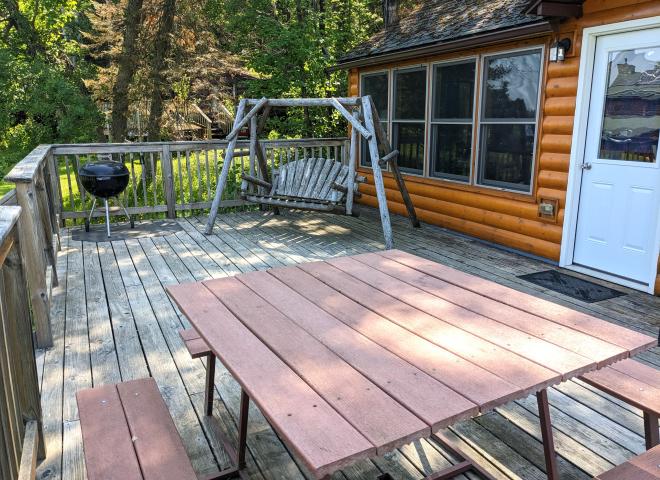 Deck area with a picnic table, charcoal grill, and swinging bench.
