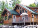 Cabin exterior with large picture windows, deck and picnic table with umbrella.