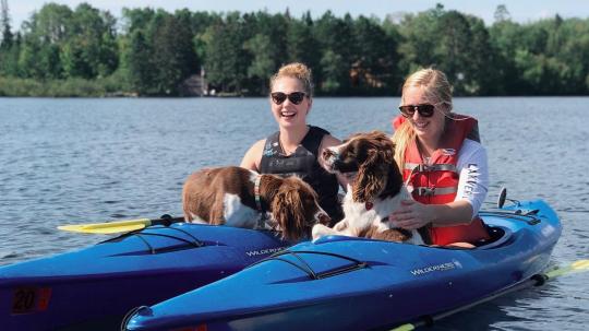 Two women kayaking with their dogs on a beautiful day.