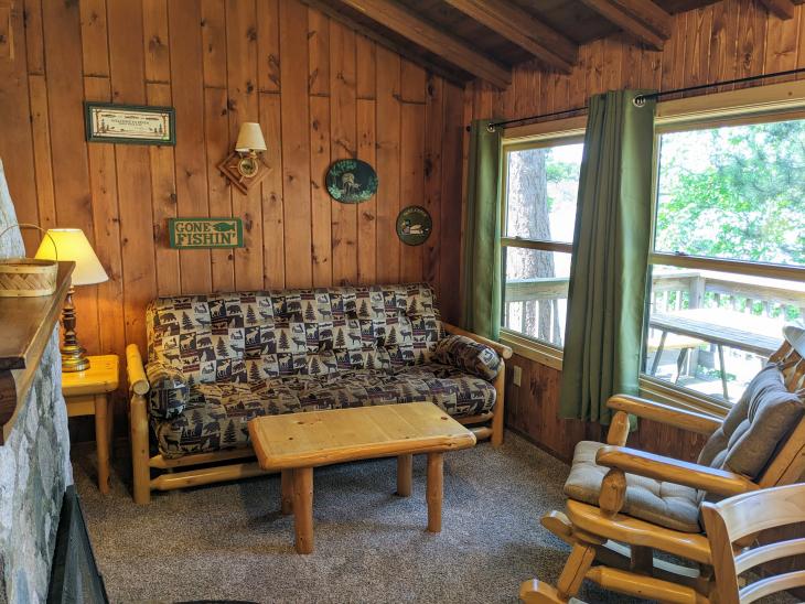 Living room with a double futon, rocking chair, and wood burning fireplace.